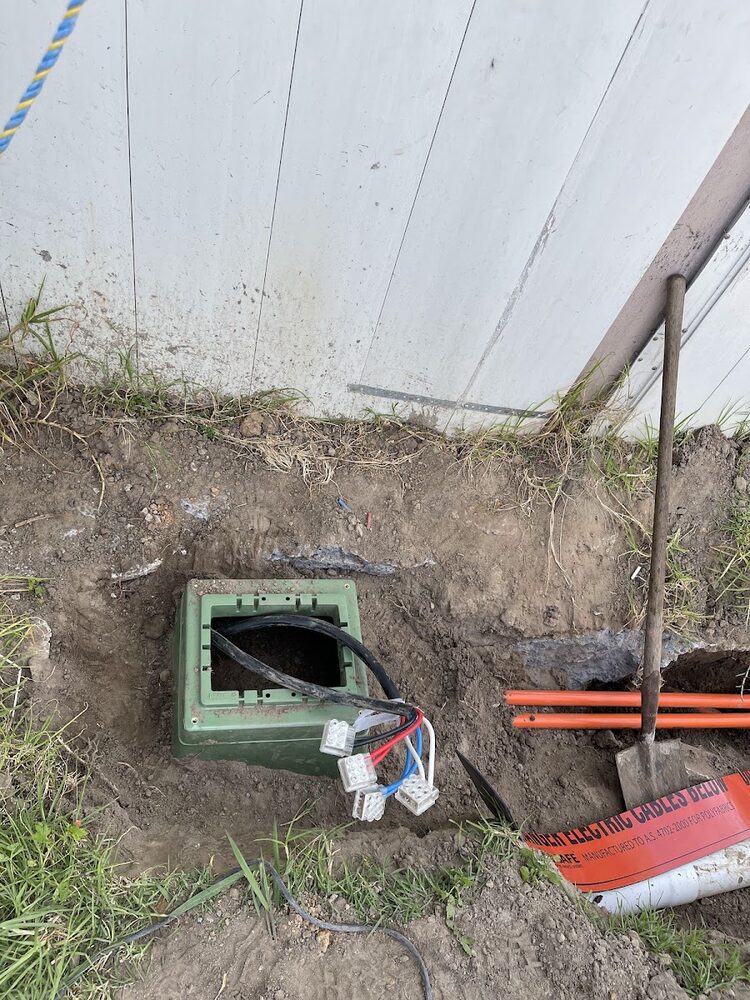 Open pit with orange conduit and cable marker tape during an underground mains run